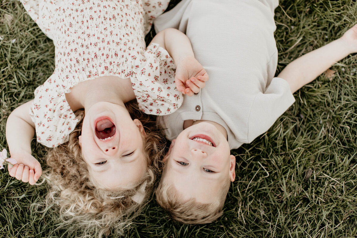 Two toddlers lying on grace laughing at each other. 