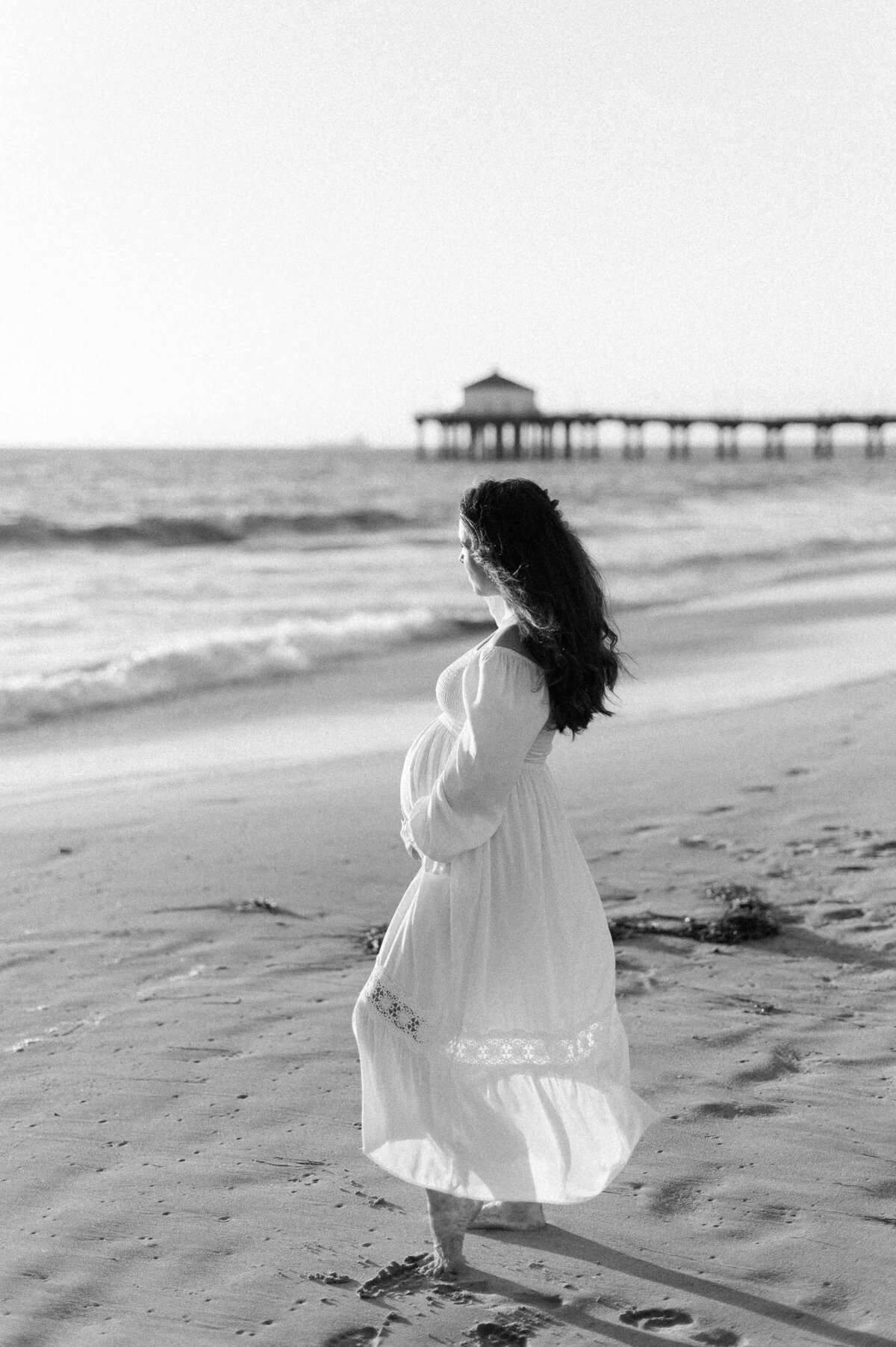 A pregnant woman posing on the beach while being photographed by a maternity photographer in Los Angeles.