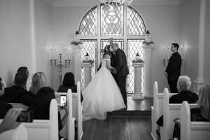 Bride and groom sharing first kiss during intimate wedding ceremony in historic St Augustine chapel with stained glass windows