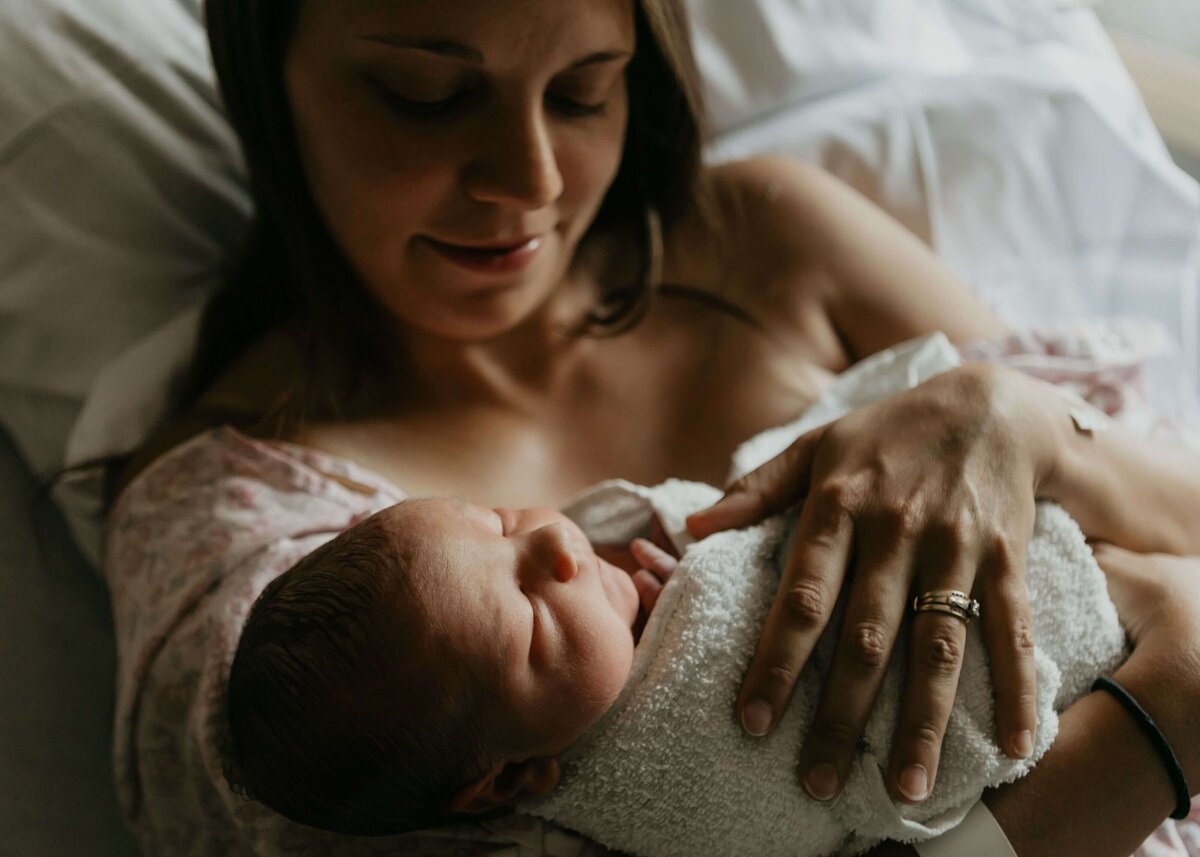 A woman cradles her newborn baby in a hospital  bed, captured beautifully by a Pittsburgh newborn photographer.