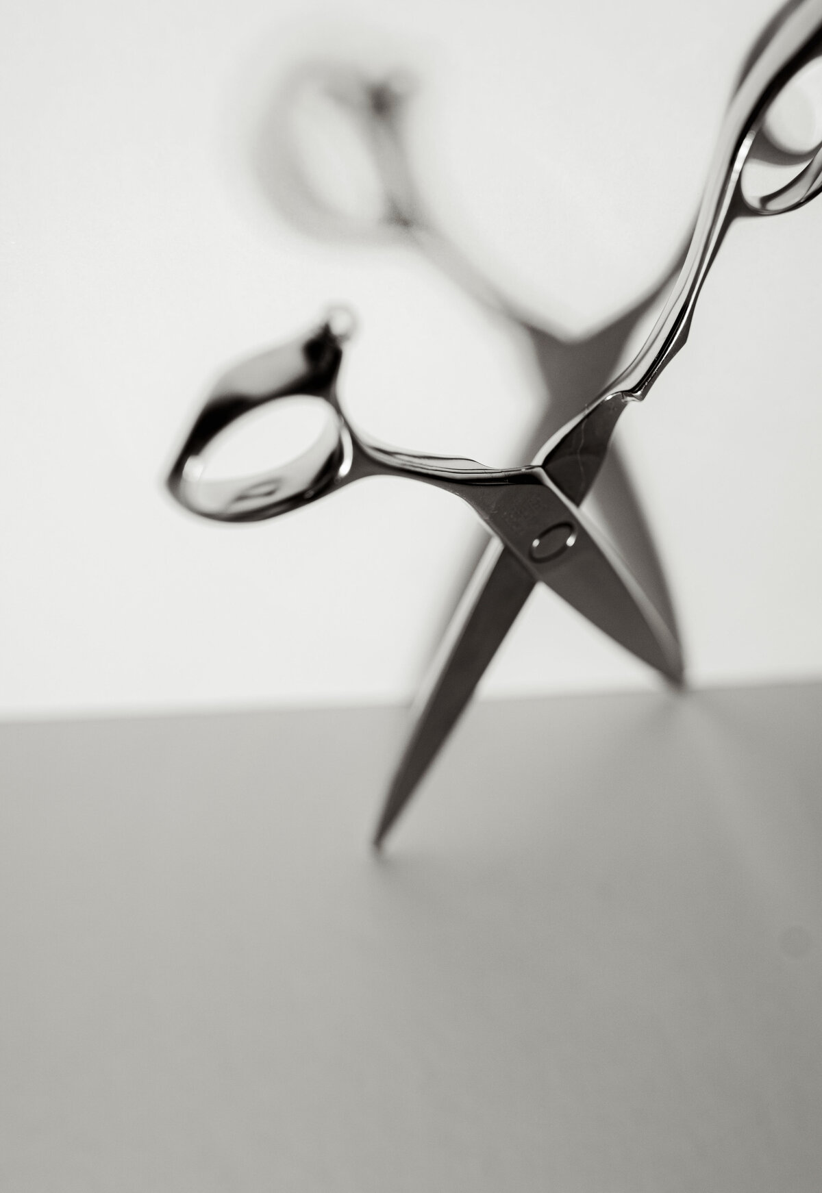 Black and white editorial image of hair-cutting shears standing upright on a clean background — modern, minimal product photography for barbers or stylists.