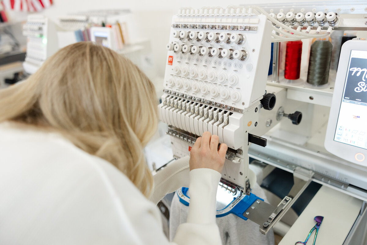 Blonde woman seated at embroidery station selecting fabric thread options. Photograph by Yucaipa branding photographer Kaitlyn Dawn Photography.