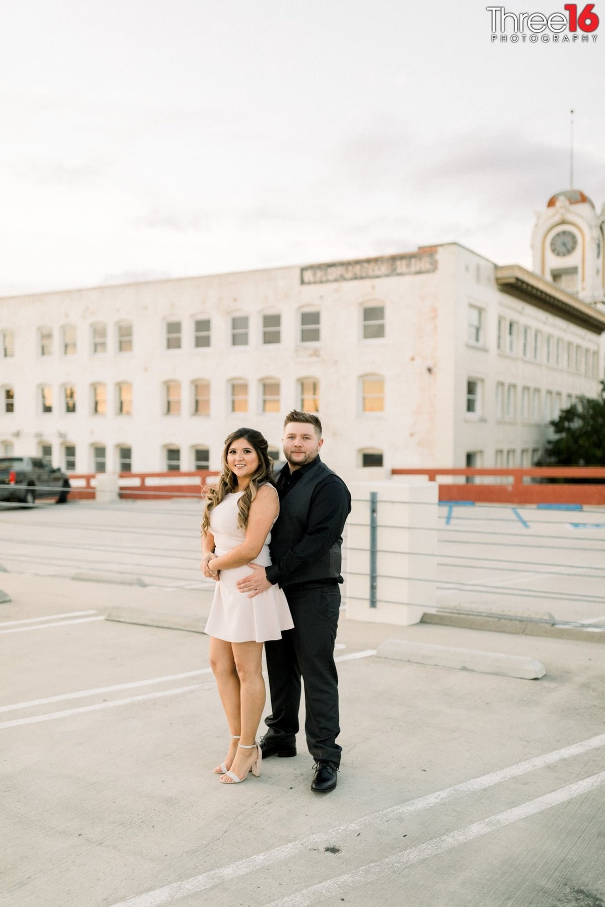 Engaged couple pose together as they stand atop of building parking lot