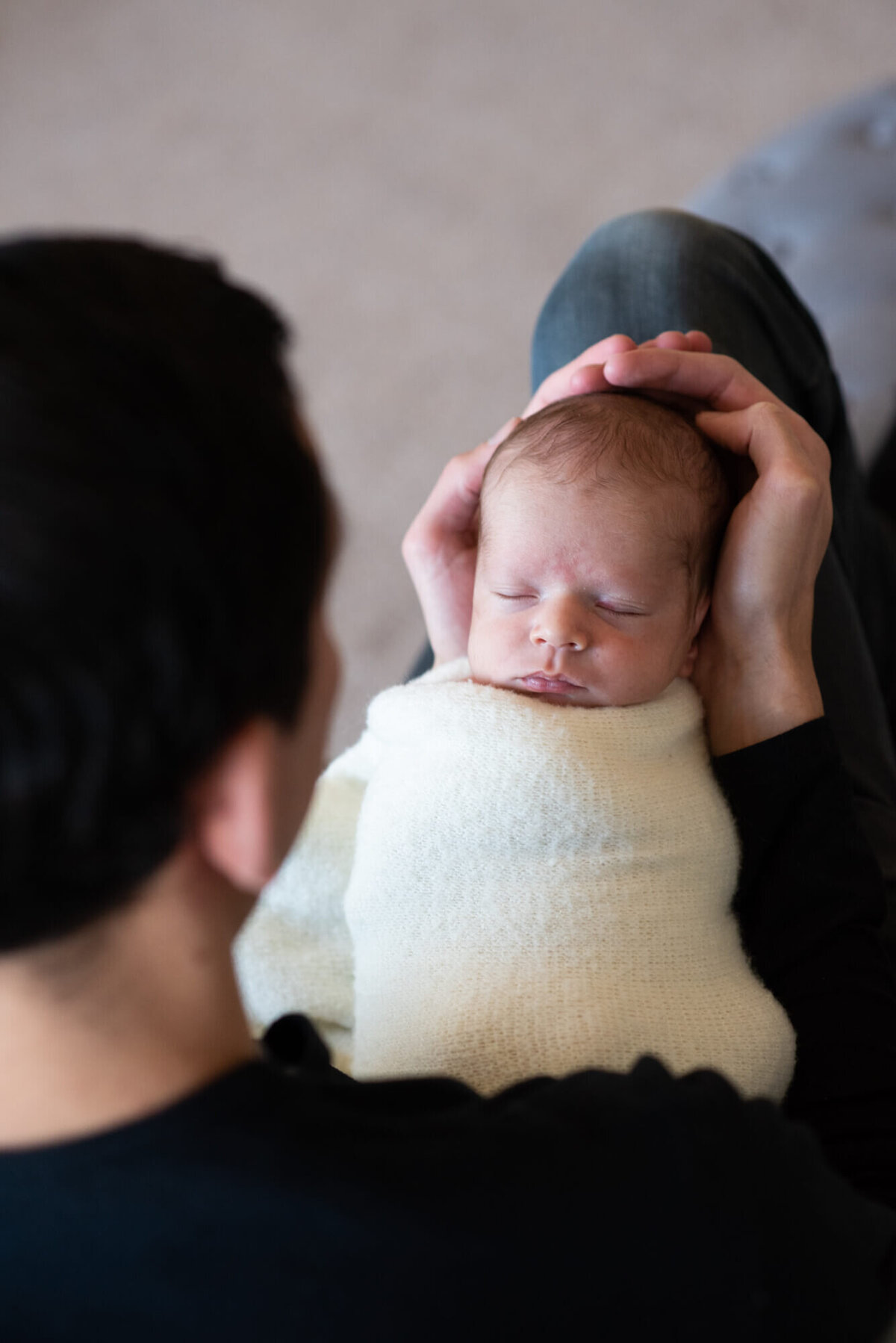 An image taken by a Denver Newborn Photographer of a newborn baby sleeping in dad's hands as he looks down at it
