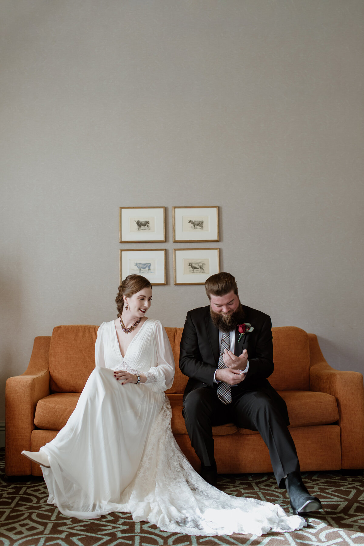 A bride and groom sitting on an orange couch making final adjustments to their clothing candidly captured by Fort Worth wedding photographer, Megan Christine Studio