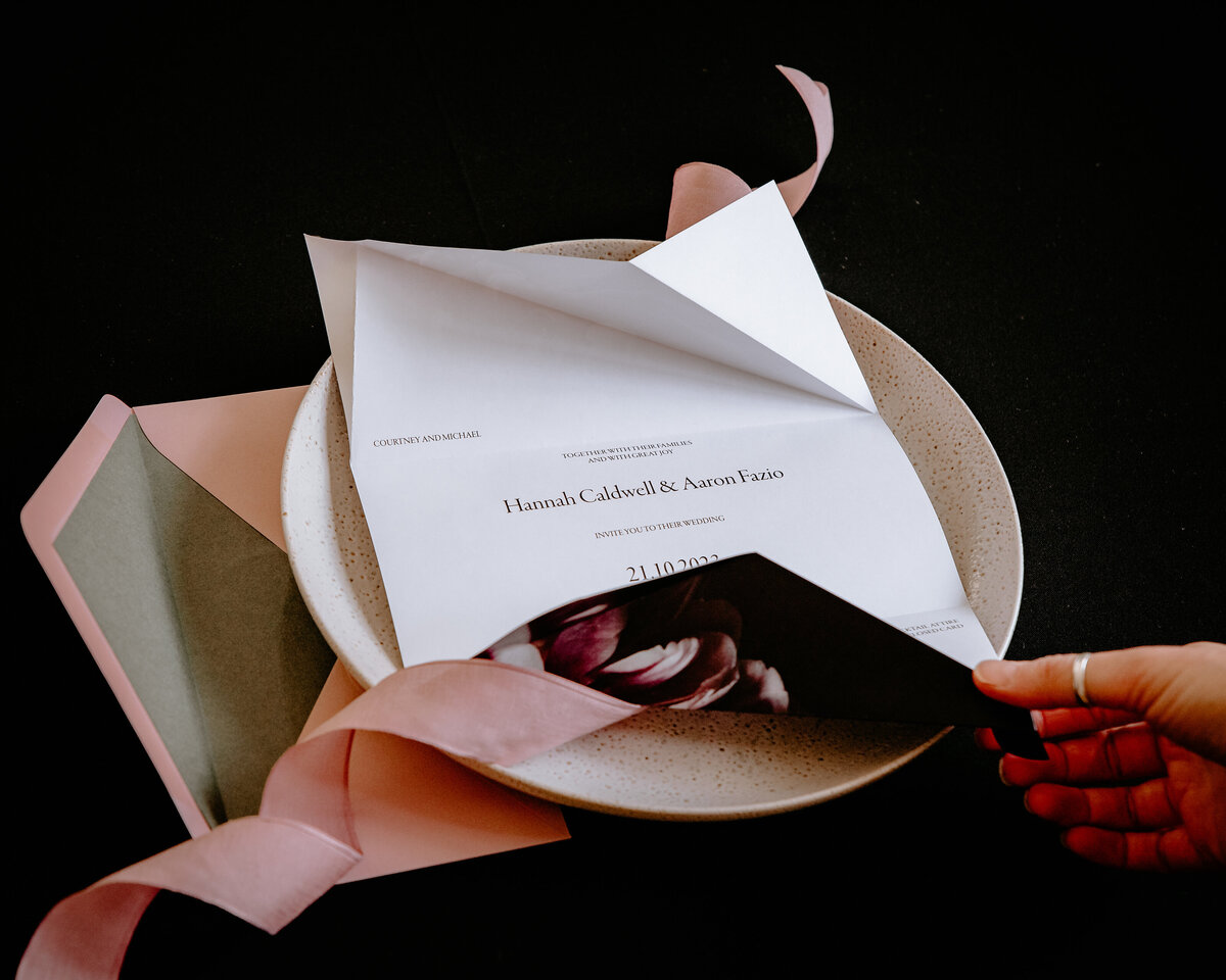 Hand holding an origami wedding invitation with minimalist design and pink and green envelope