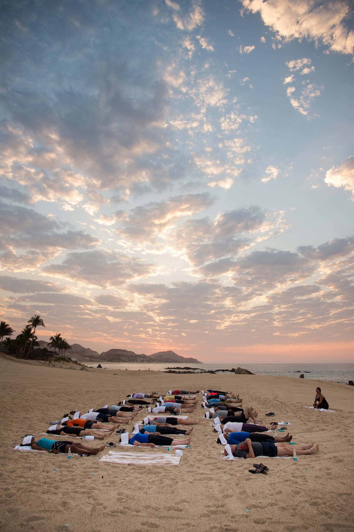A Yoga Class lays down in shavasana on beach in Hawaii