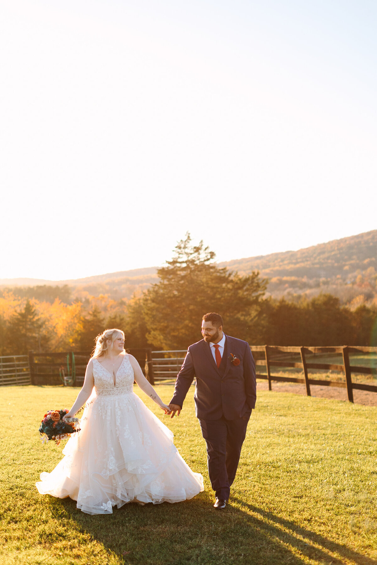 Bride and groom walking holding hands through a field during their fall, Virginia wedding