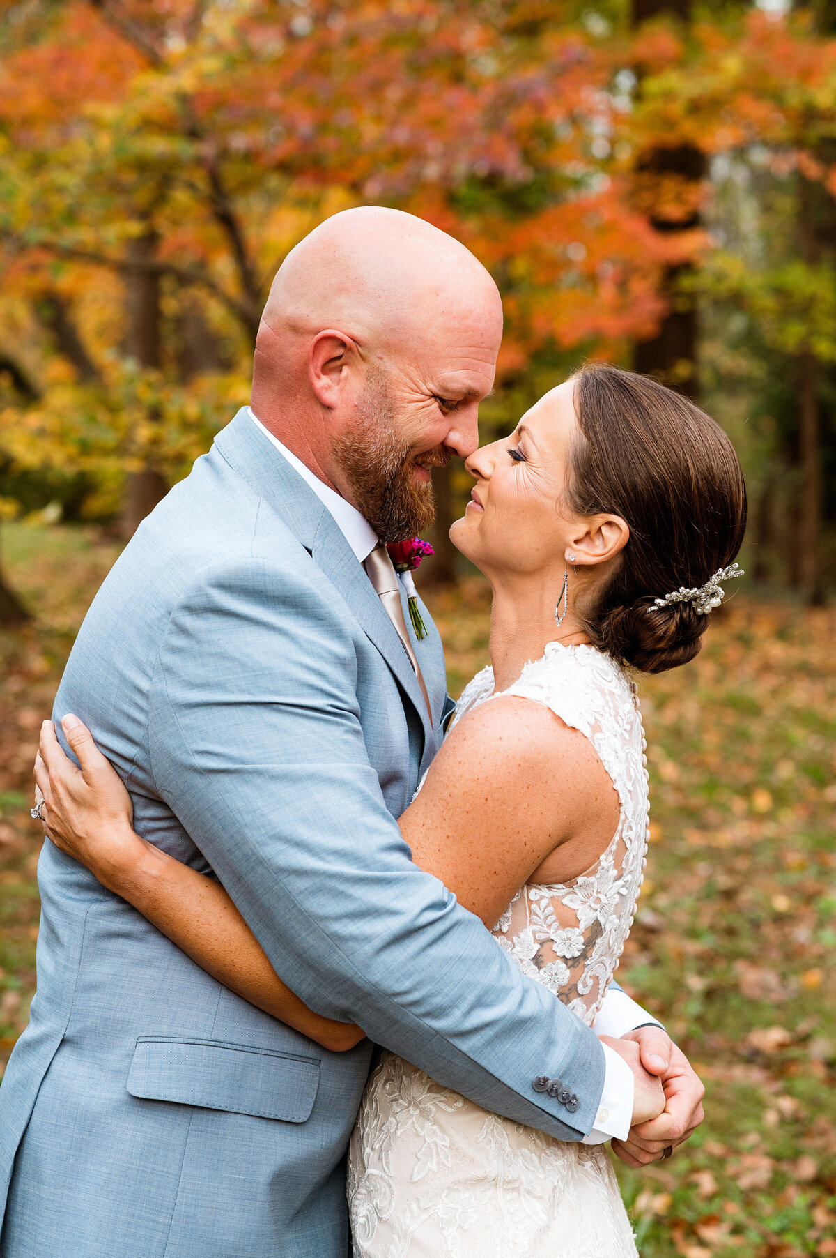 Newlyweds snuggled together smiling at each other with fall colors behind them