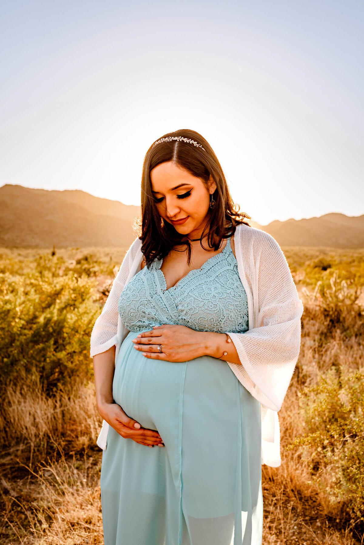 pregnant mother with blue dress holding her maternity belly during her photography session in Arizona