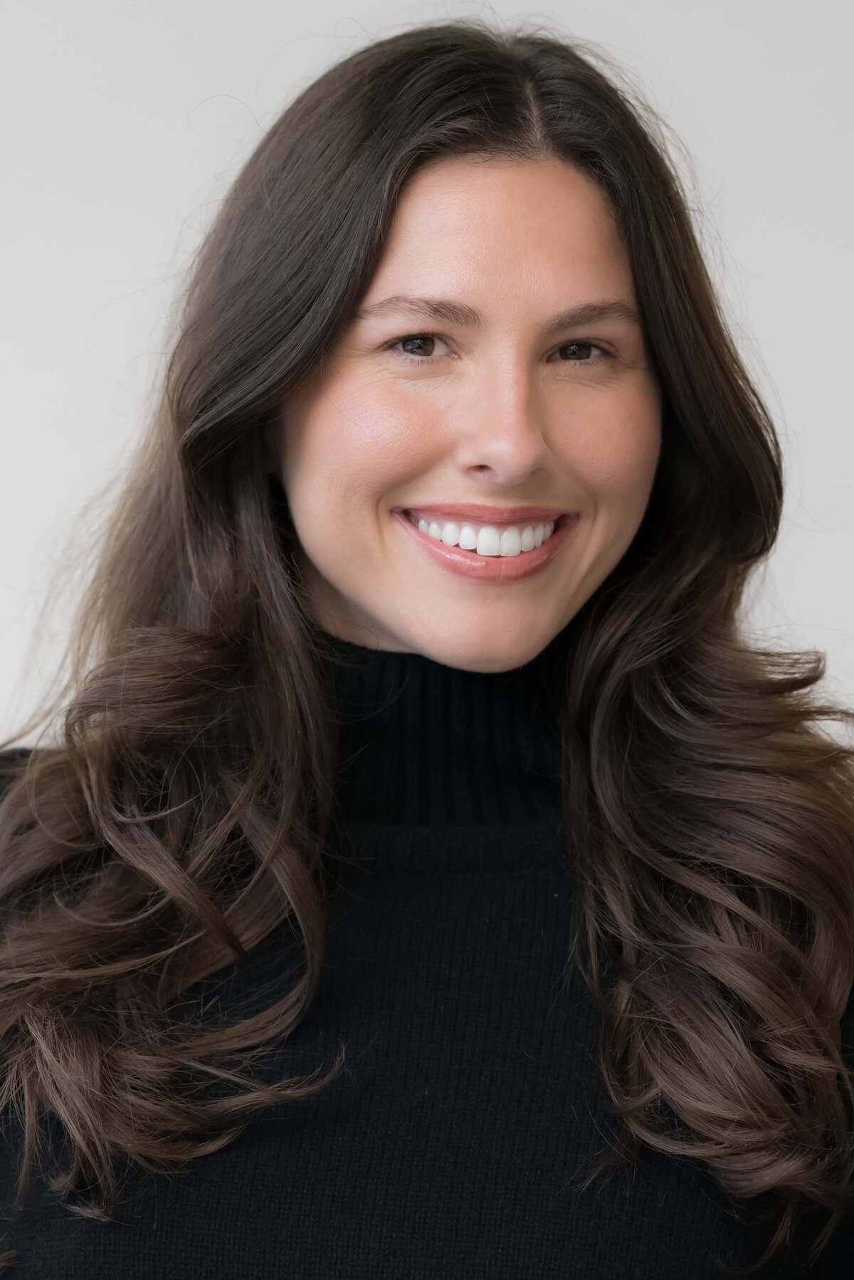 young woman with dark hair smiling while wearing a dark sweater posed for a modeling headshot