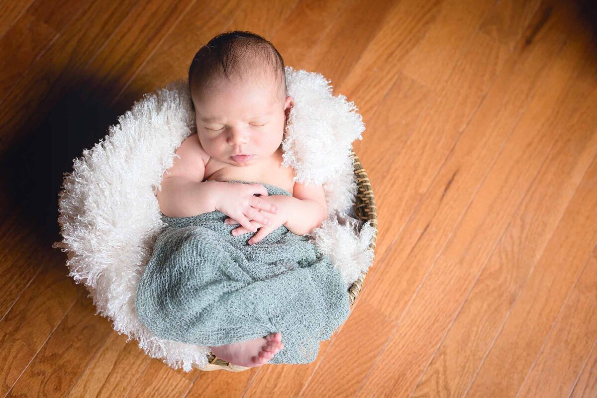 Cute little newborn in a green wrap snuggled in a blanket in Columbia, SC