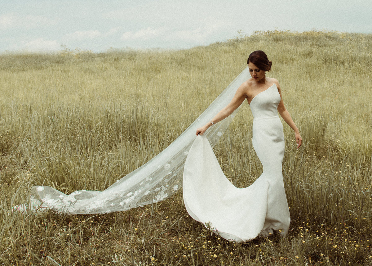 bride playing with her dress in a field