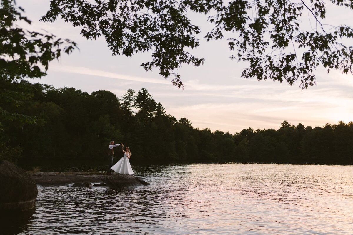 bride and groom dancing by the lake during sunset