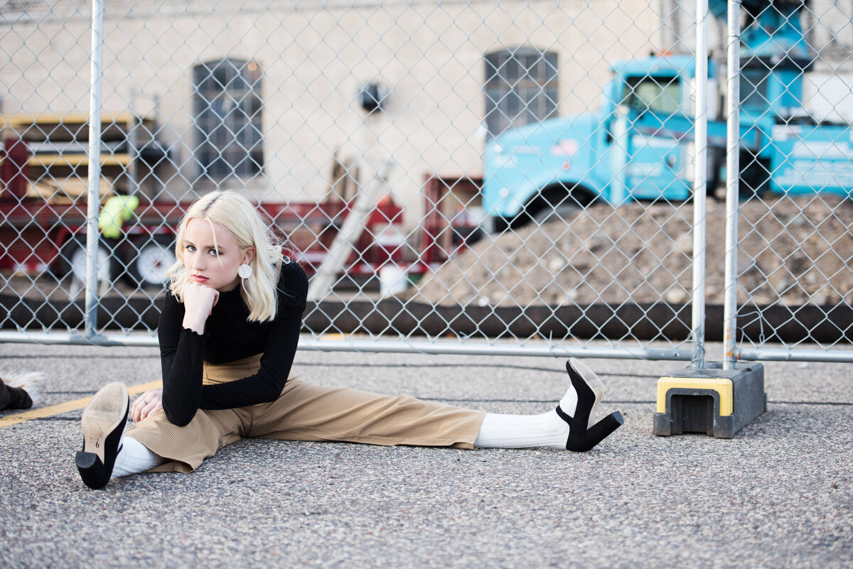 Blaine Minnesota high school senior photo of girl in fashion outfit sitting in front of chain link construction area