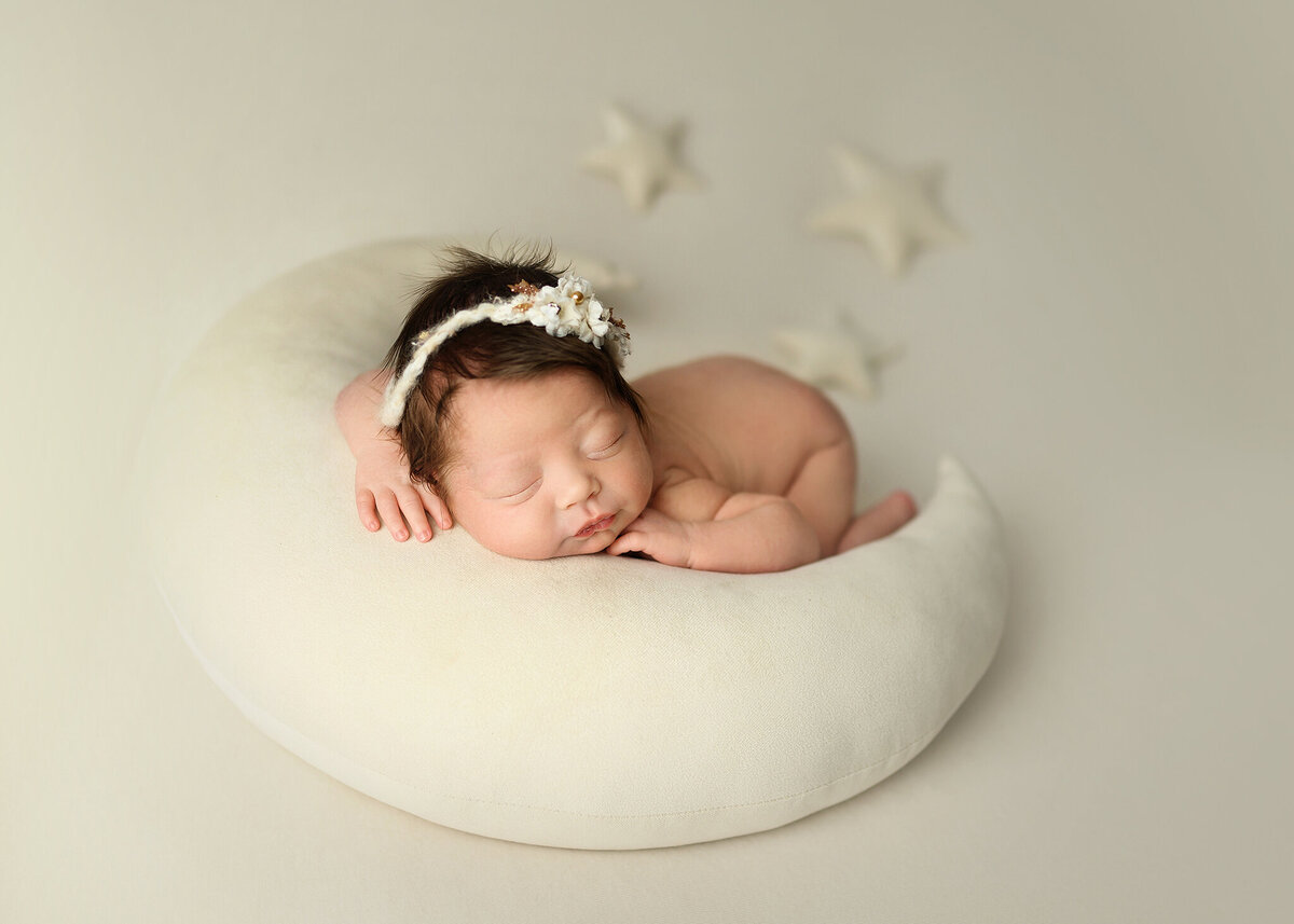 sweet little baby girl comfortably sleeping on a soft moon prop with star accessories on white background