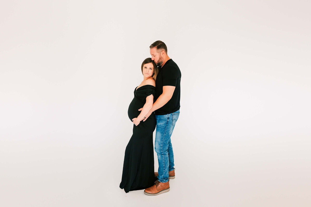 pregnant mom in black gown kissed by her husband during Springfield MO maternity photography sesssion