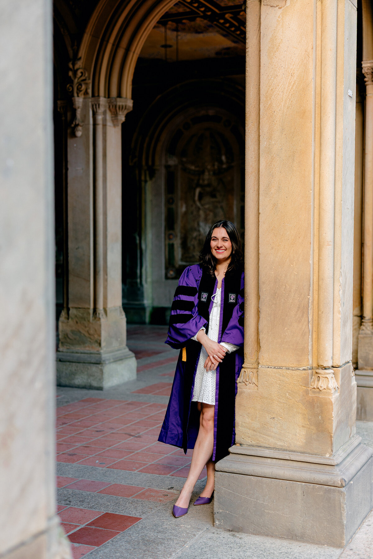 NYU graduate smiling in purple gown during portraits at Central Park.