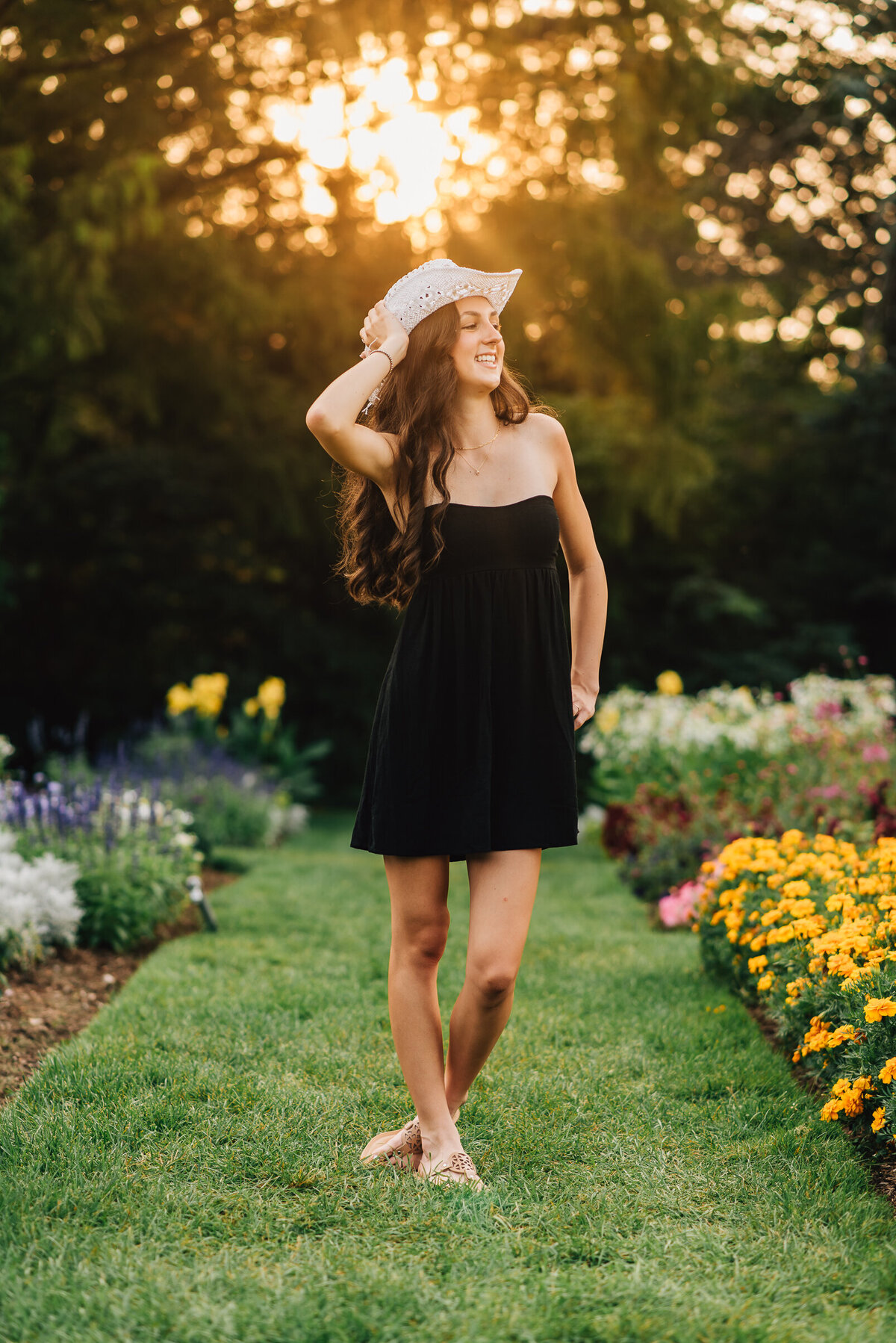 High school senior girl looking up at the sky in black dress with white cowboy hat