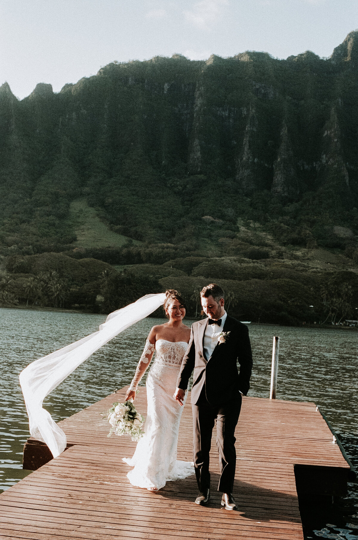 Elopement Photography, bride and groom walking on a dock with kualau mountains in the background while veil flows in the wind