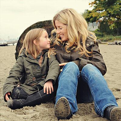 Mom and daughter casually sit at the beach in the fall smiling in Vancouver