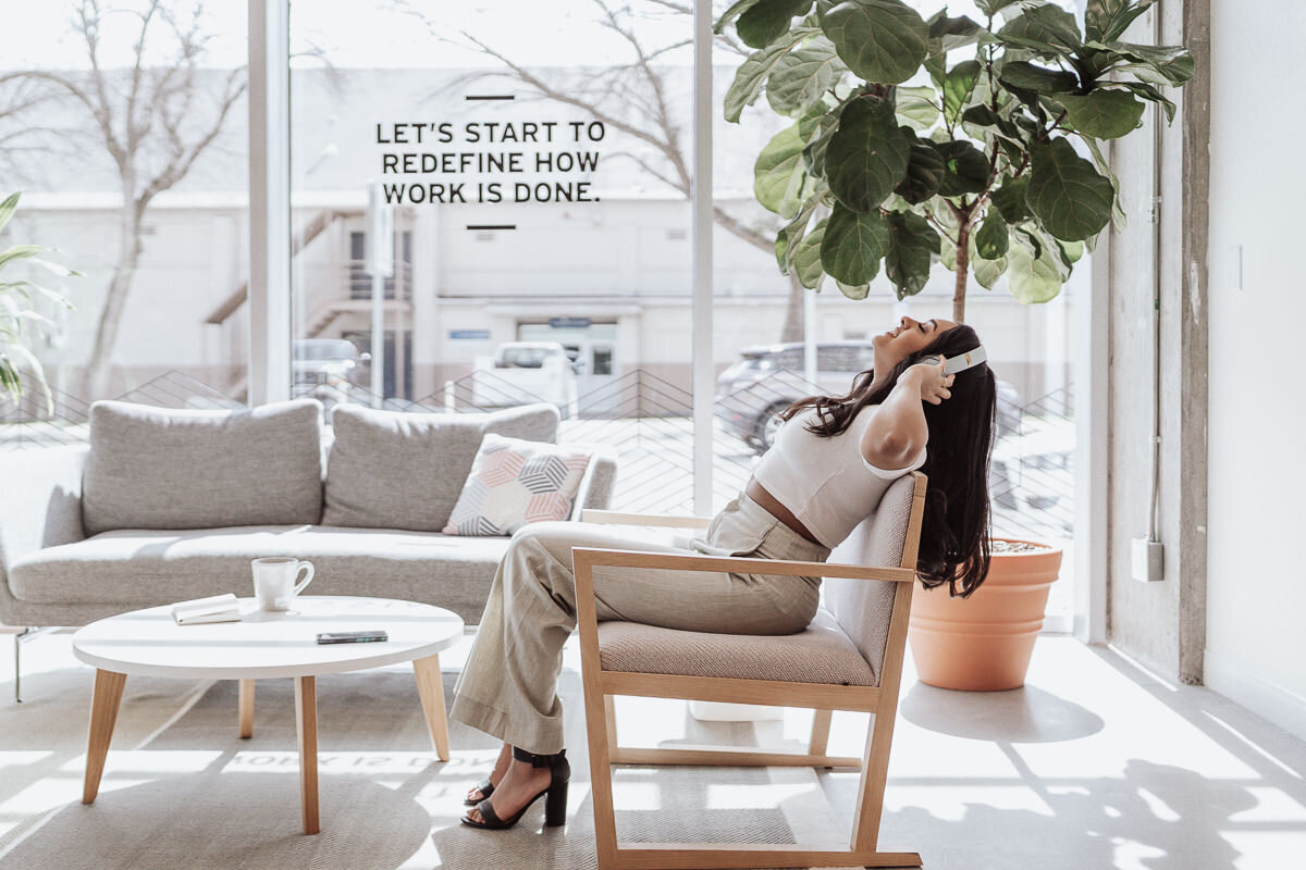 business woman listening to headphones in cream suit in modern office setting