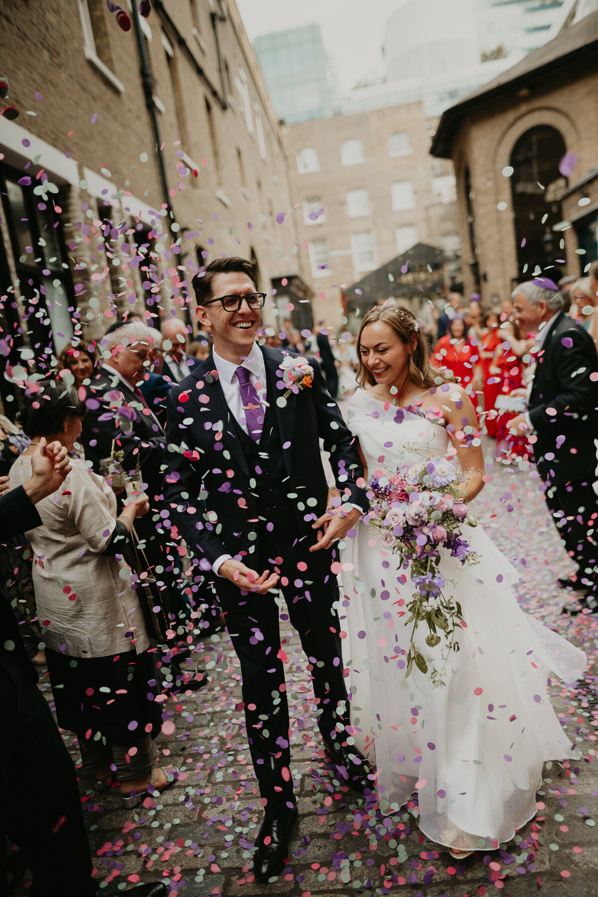 Bride and groom walk through The Brewery in London as their wedding guests throw confetti. 