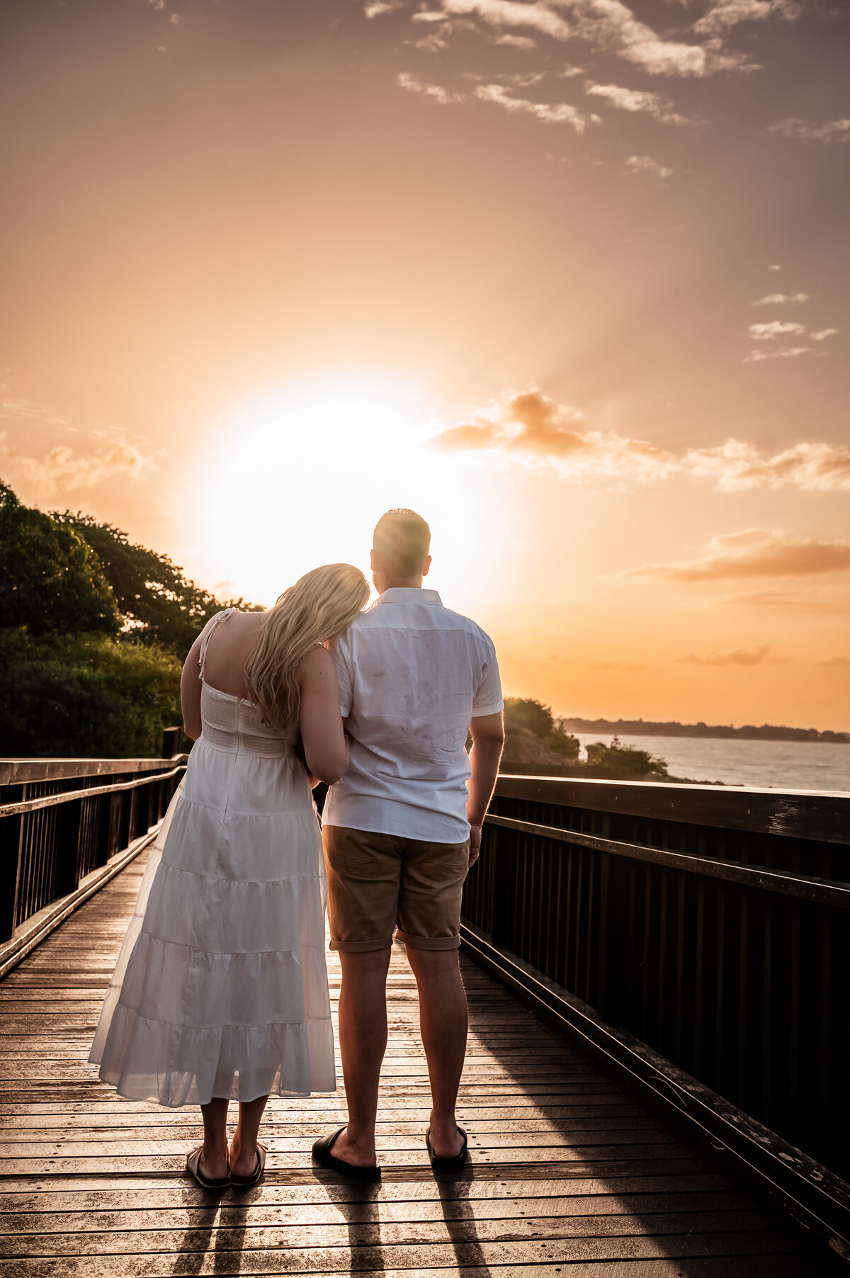 man and woman embracing on a boardwalk while watching the sunset - Townsville Engagement Photography by Jamie Simmons