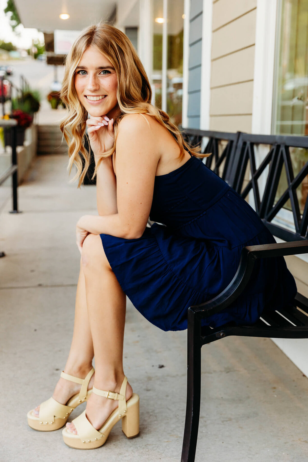 senior girl in a navy blue dress leaning forward while sitting on a bench