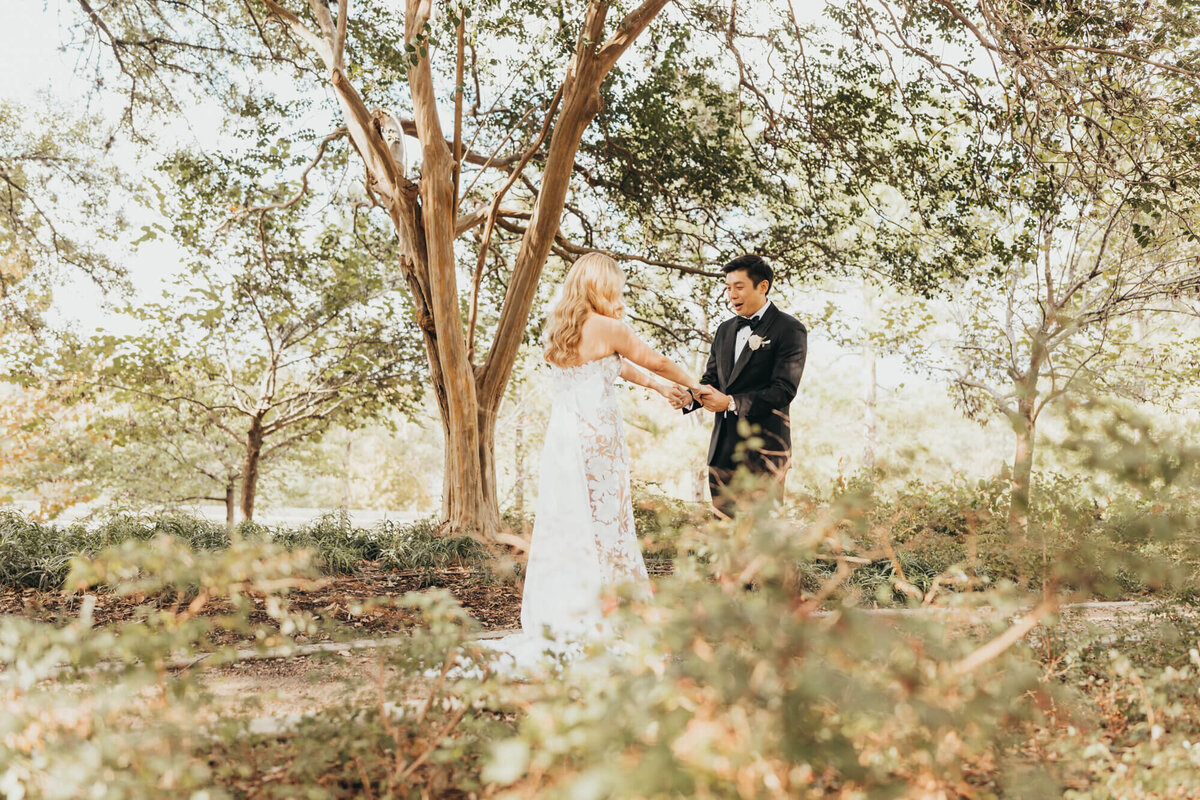 groom adores his soon to be wife during their first look under trees.