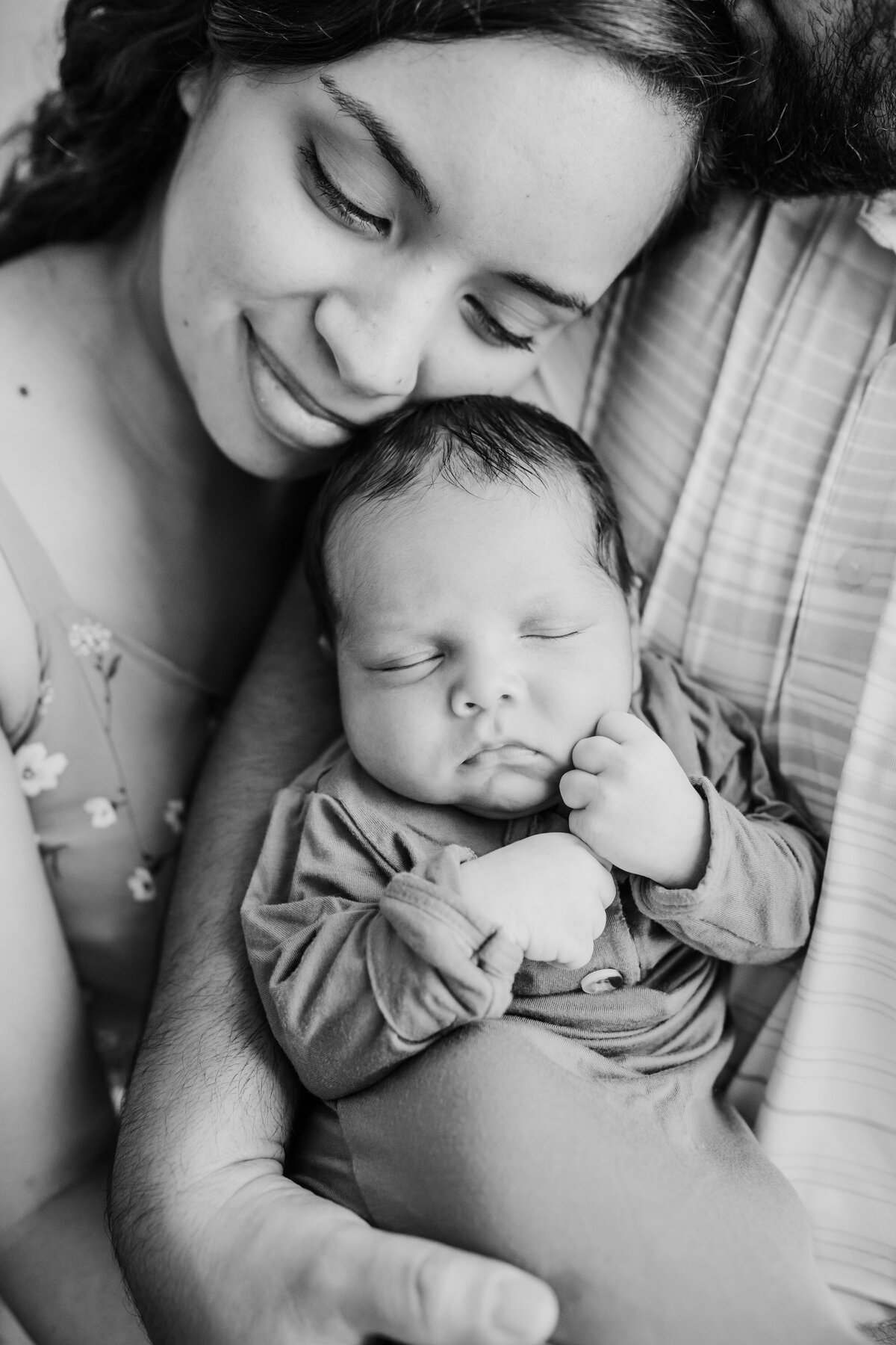 Newborn Photographer, a young mother leans on her husband as he holds baby in his arms