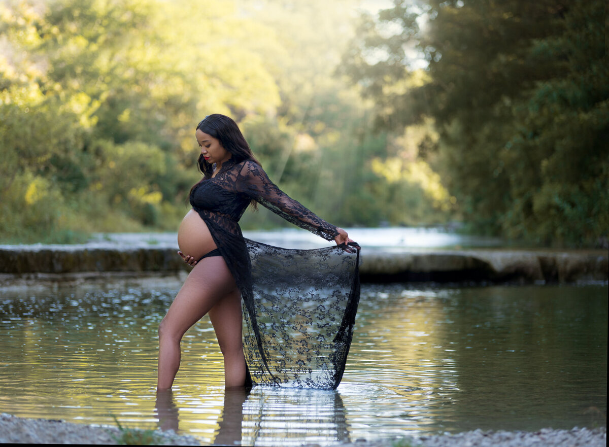 Pregnant woman in sheer black lace robe standing in a creek at Cedar Park maternity session