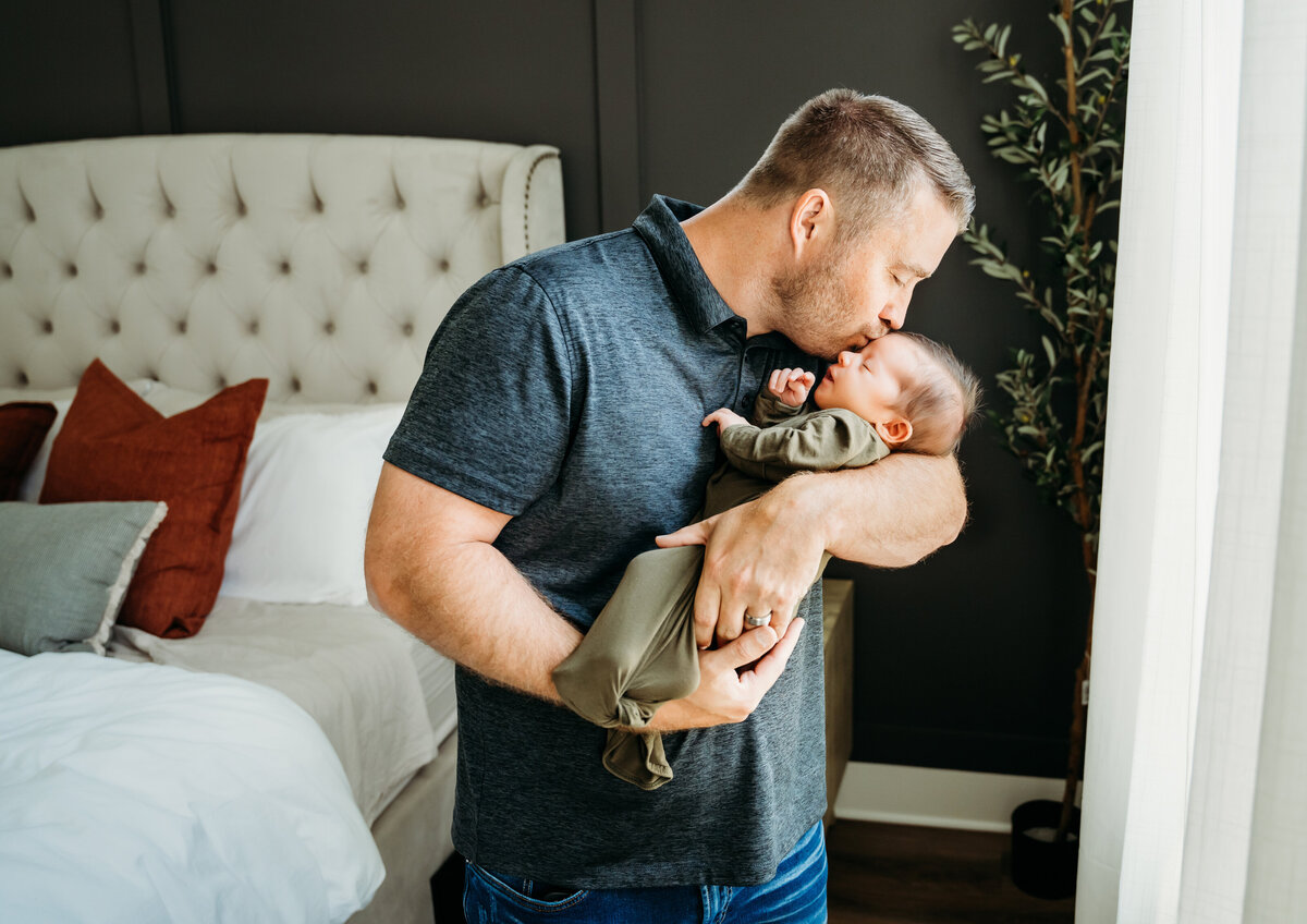 Newborn Photographer, a father holds newborn baby and gives him a kiss in bedroom