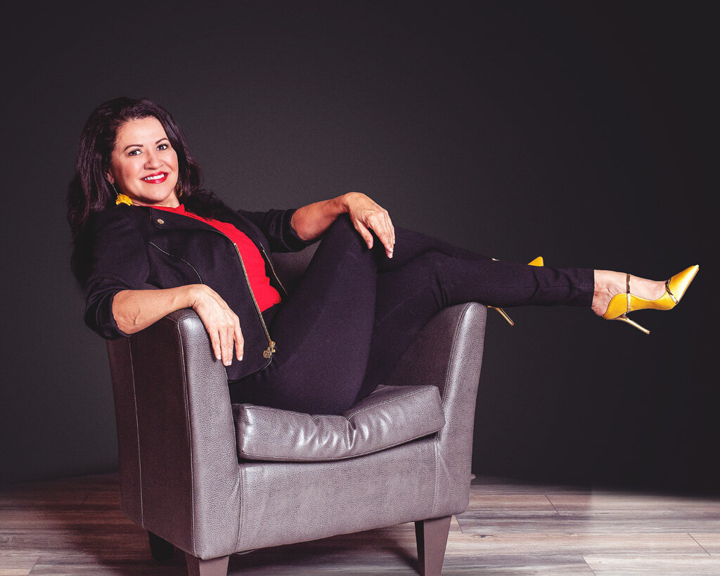 branding photo of a woman sitting sideways in a chair with black pants red top and yellow shoes