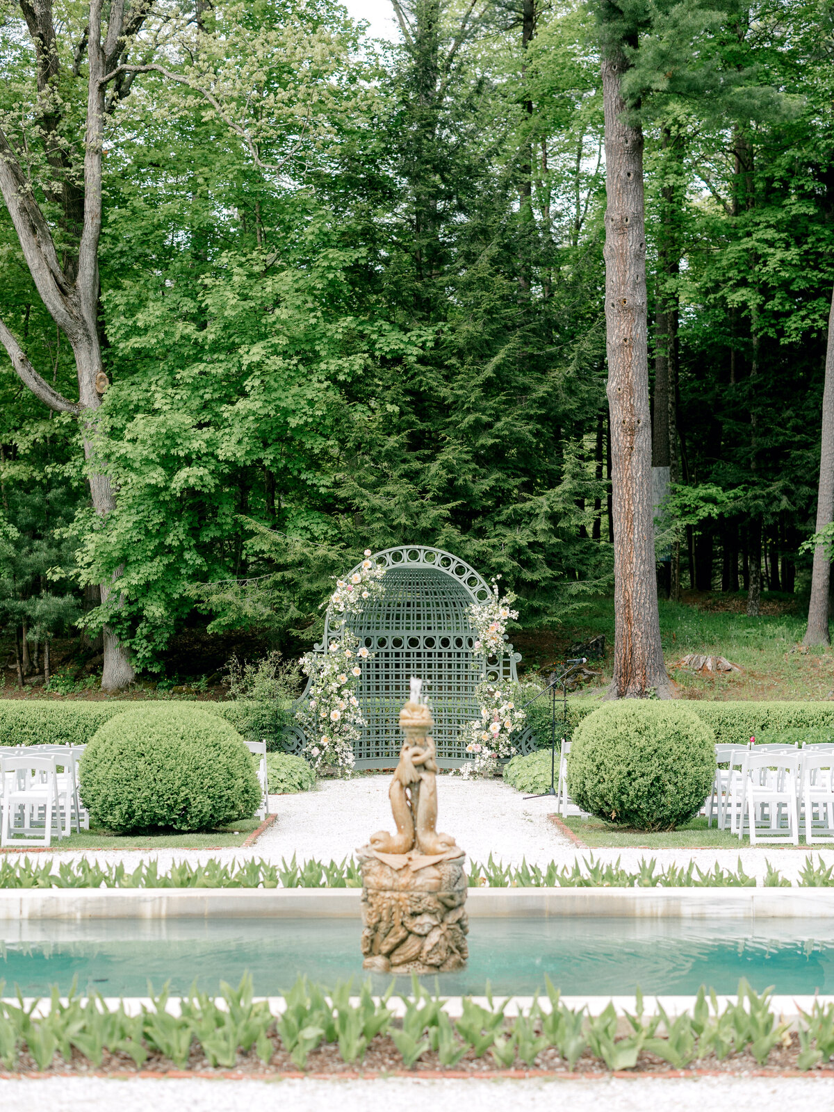 Floral wedding ceremony arch in New England with a pool and fountain in front of ceremony arch.