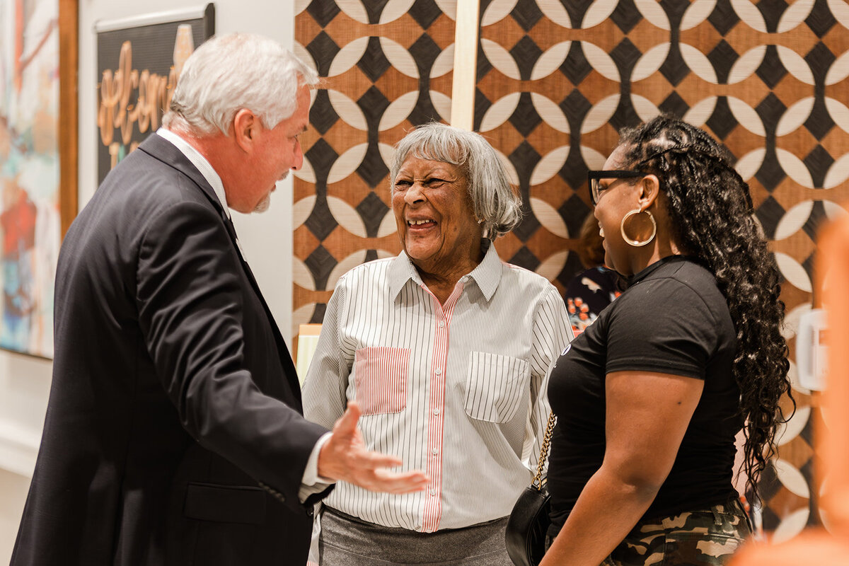 Three people conversing happily in a grand opening event with colorful geometric patterns in the background. two women and one man engage in friendly discussion.