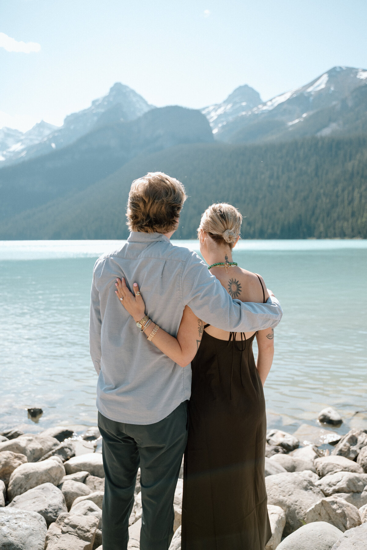 Engaged couple sitting on stone ledge at Lake Louise with peaceful water and sky.