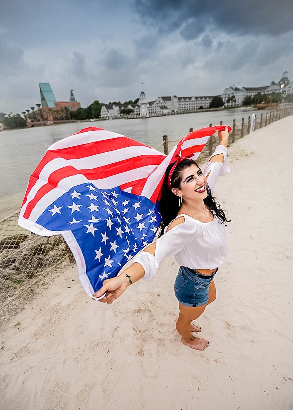 Woman holding an American flag for 4th of July, flag blowing in the wind, standing on the beach