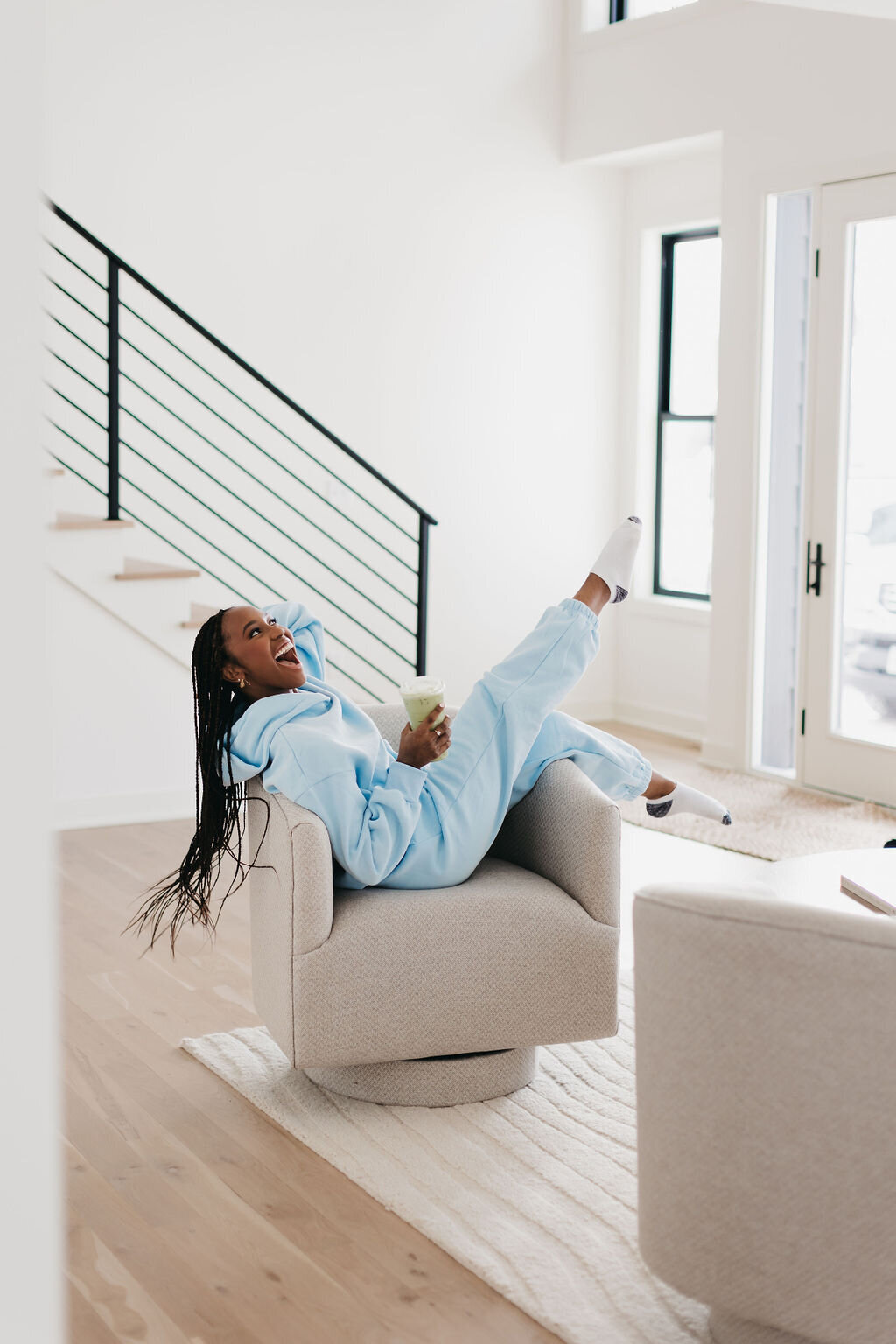 Juma Waganda sitting sideways in a chair with her legs up wearing a light blue sweatsuit and holding a matcha