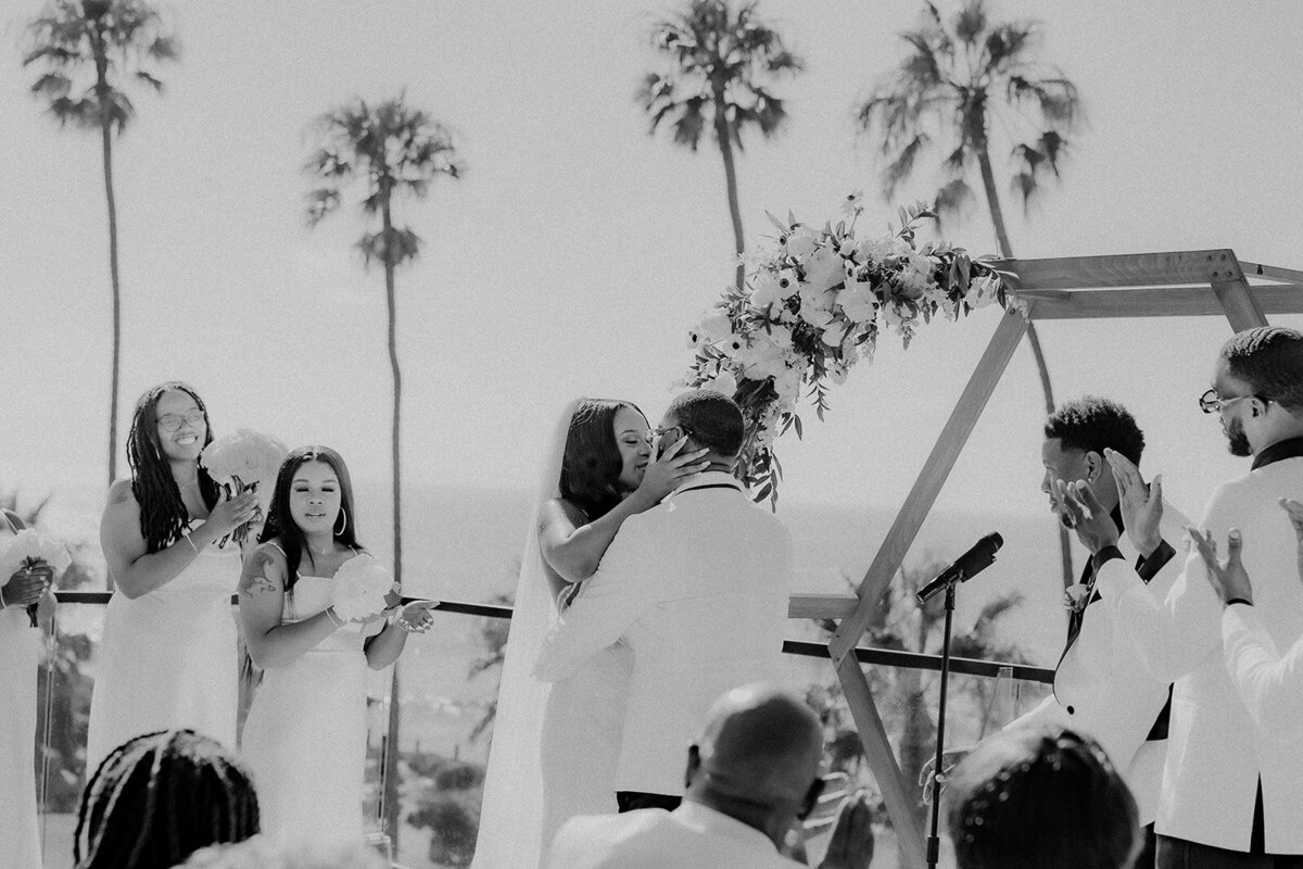 Bride and groom kissing at the alter and wedding party clapping in San Diego