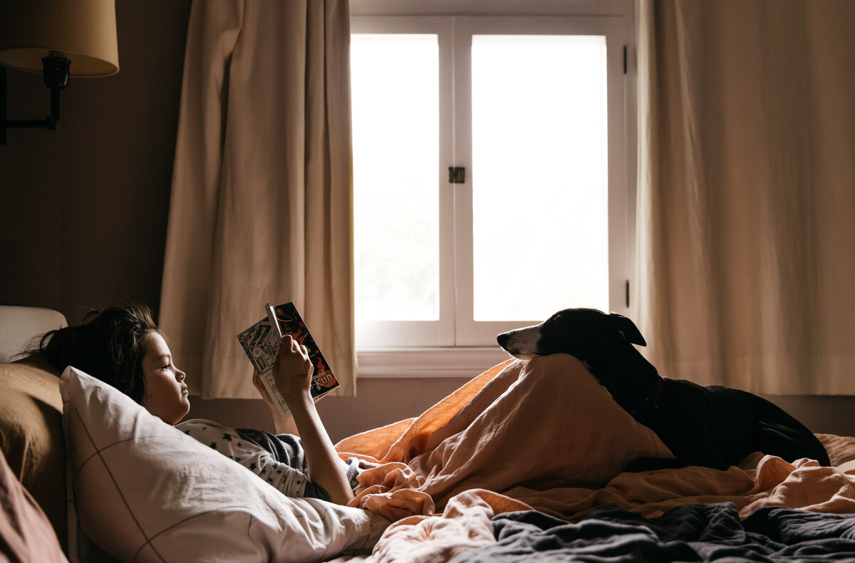 Teenager is siting in bed with their dog resting its head on their lap. 