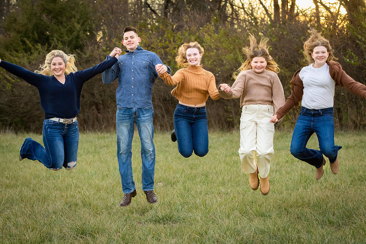 cousins jumping in a field while holding hands