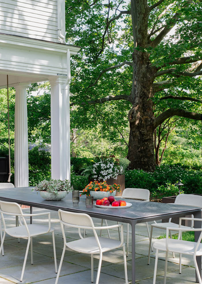 The new modern patio features stacked bluestone pavers, a Gloster dining table, metal chairs, and corten steel planters, all overlooking a mature garden. As seen on Boston Home Magazine's Instagram.