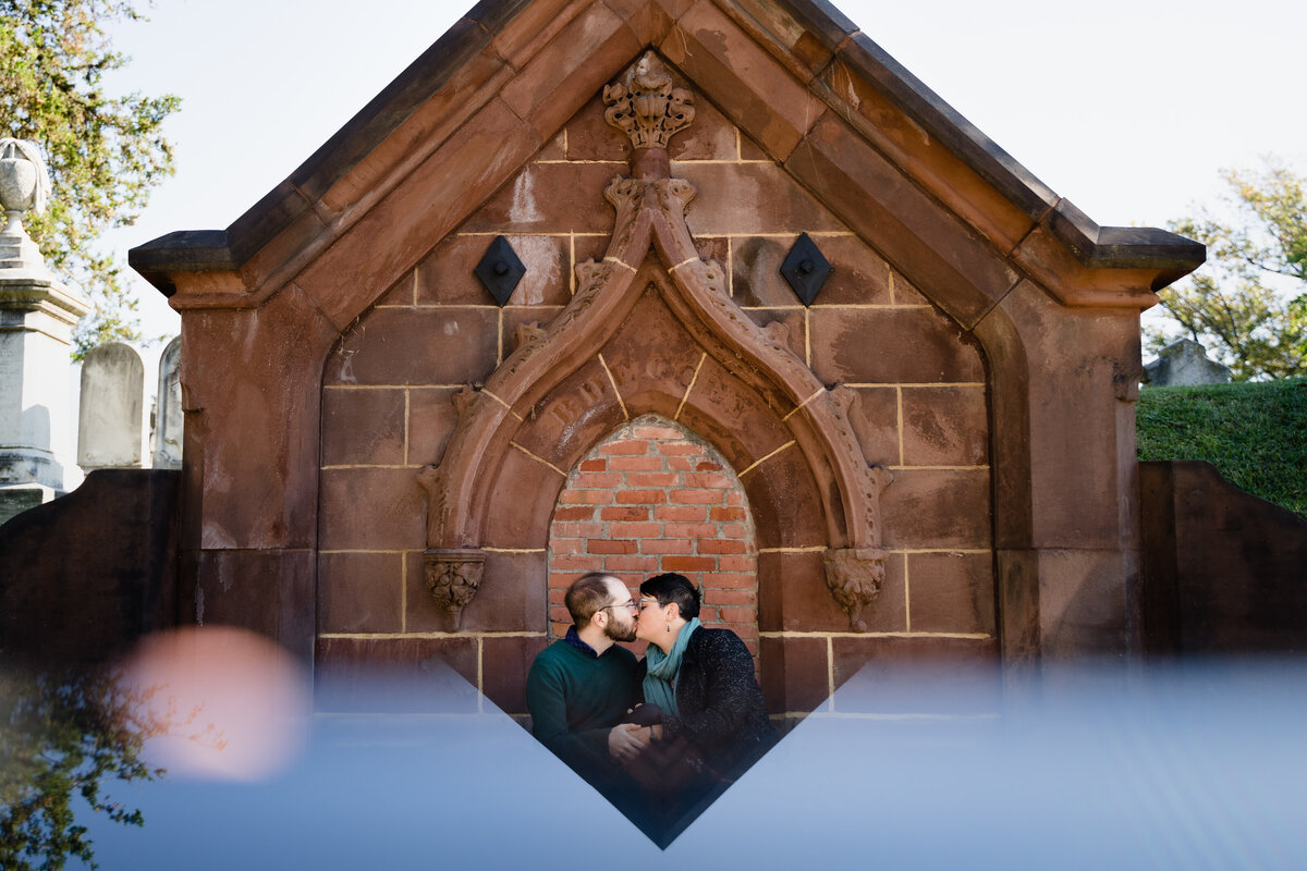 A couple kissing while sitting in front of a stone building.