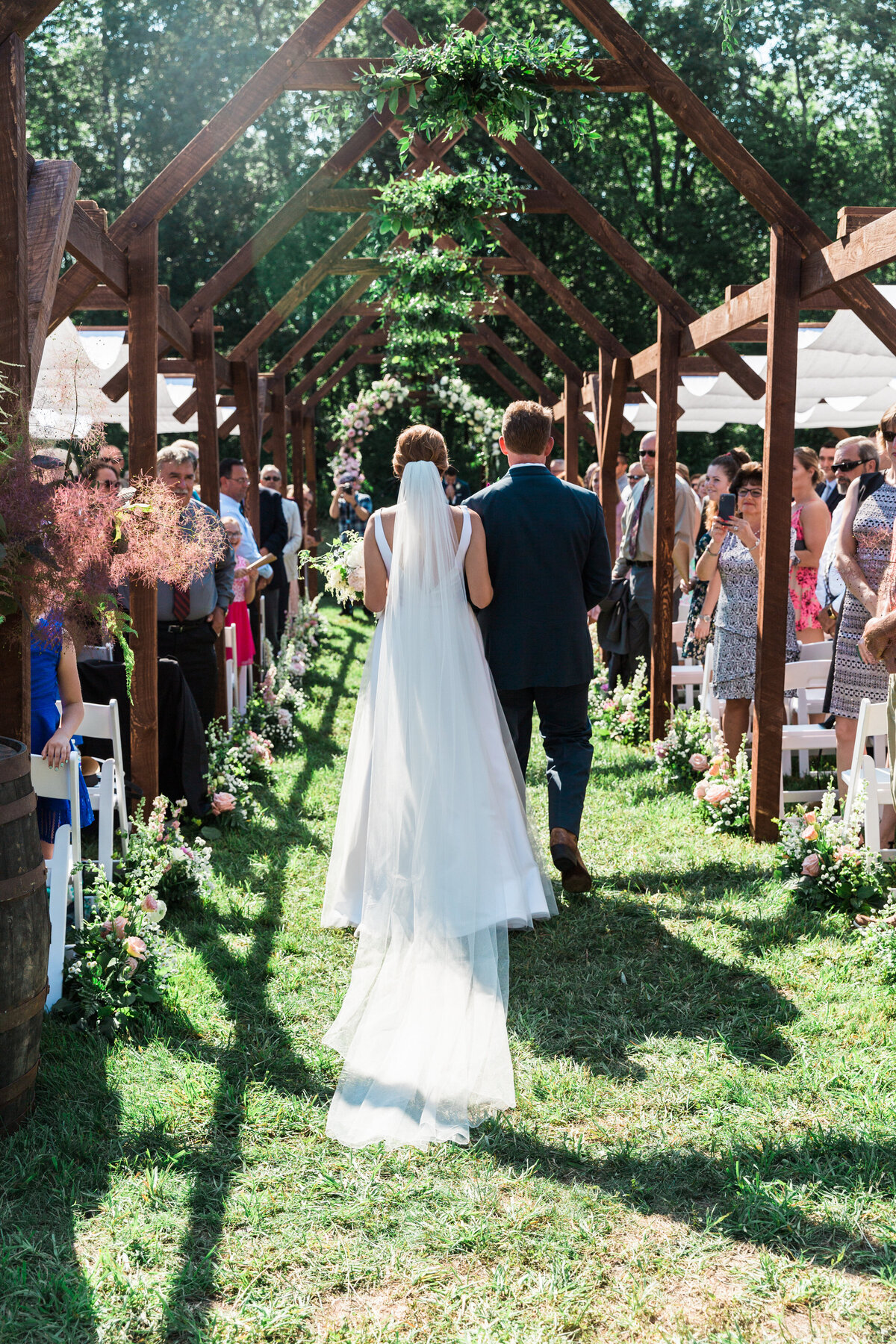 Bride and her father walking down the aisle underneath wooden arches