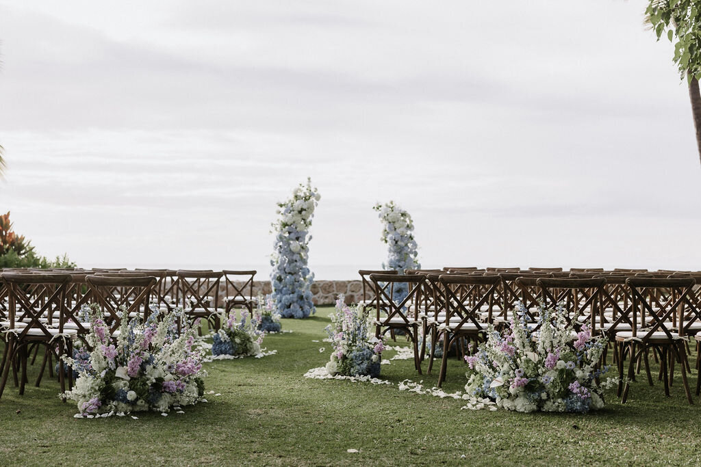 Serpentine ceremony set up of blue and purple florals at lanikuhonua in front of the ocean