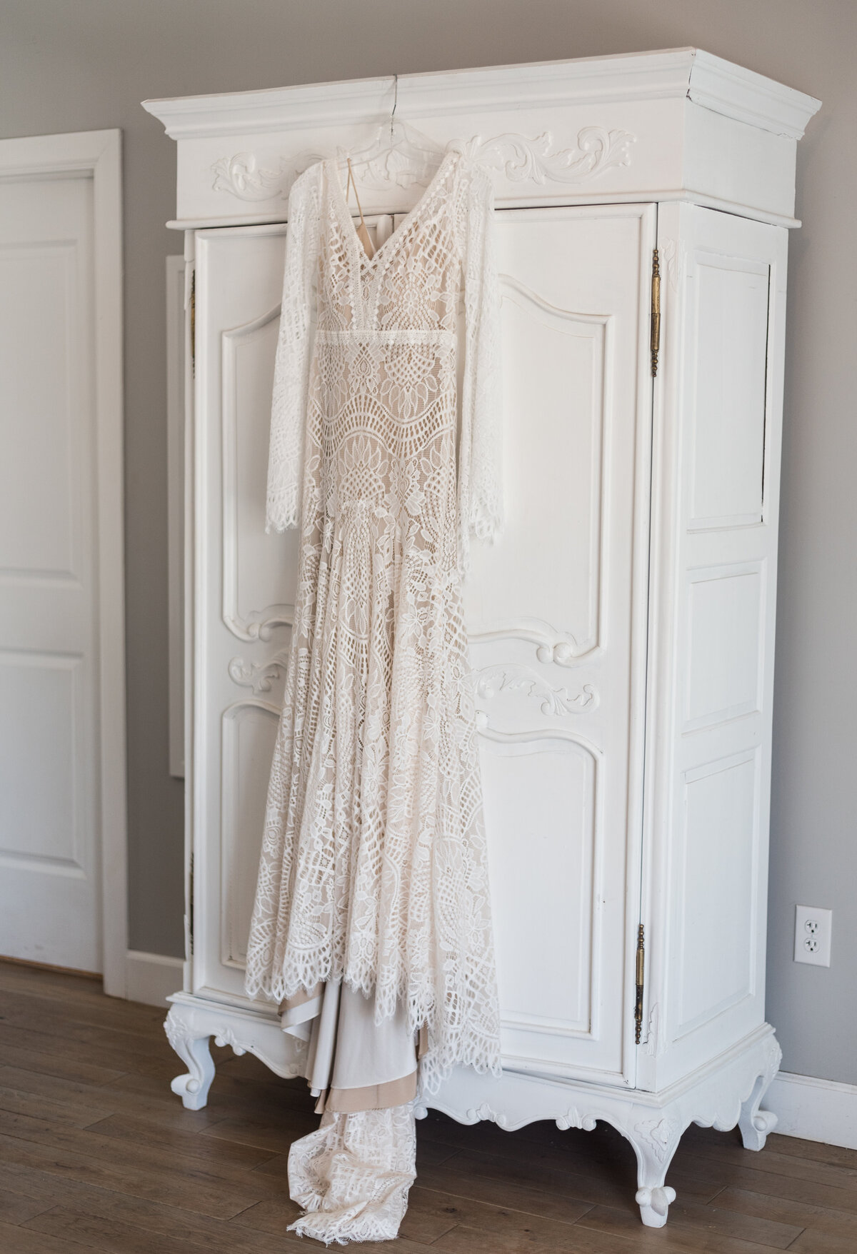 lace wedding dress hanging from a large white dresser in a bridal suite captured by denver wedding photographer