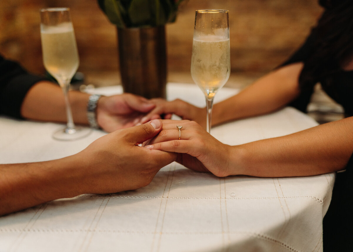 How to plan your proposal in Austin  couple holding hands next to glasses of champagne