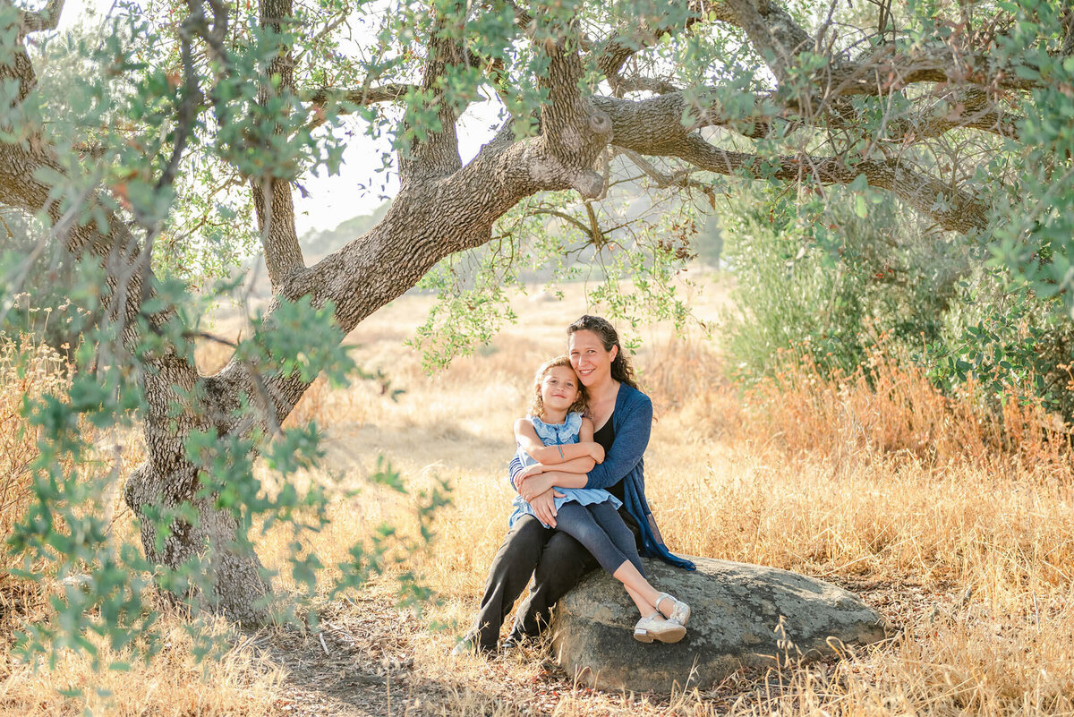 Woman sitting on a rock under an oak tree, holding her daughter