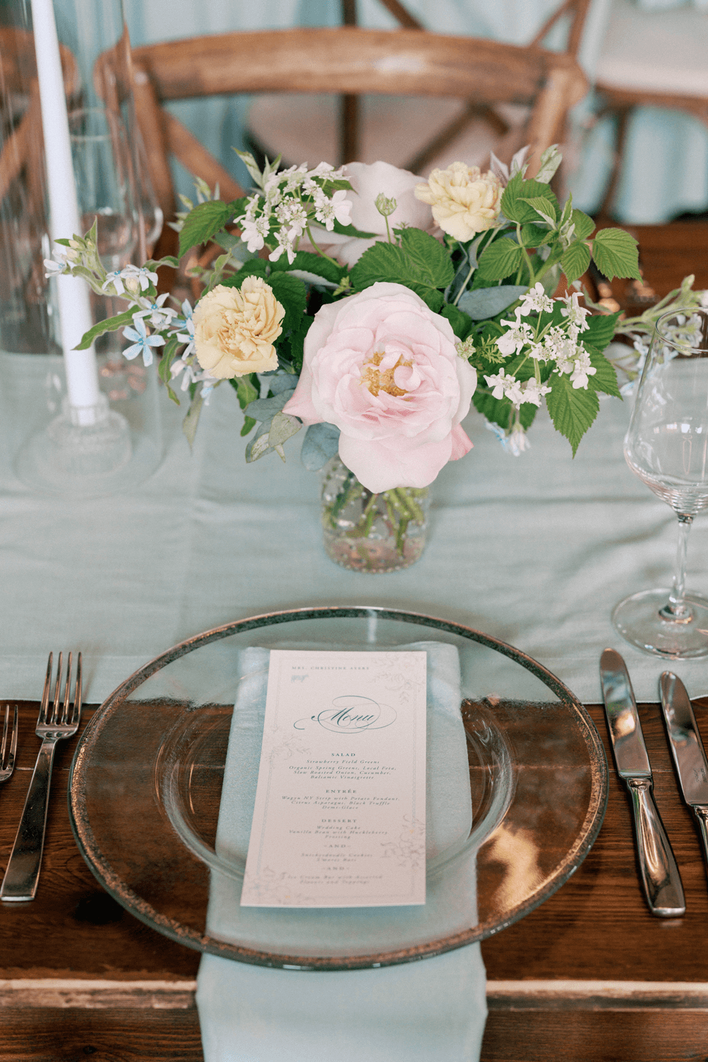 Pastel summer wedding table setting featuring a clear glass charger, floral menu, and delicate floral arrangement at Moonlight Basin.
